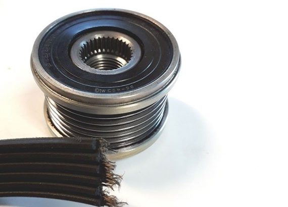 Nærbillede af en remskive og en slidt, flad sort rem på en hvid baggrund.